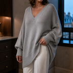 Grey V neck jumper in a close three quarter view showing the ribbed neckline cuff and draped hem.